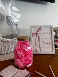 pink tissue paper is in a glass jar next to some writing utensils on a table