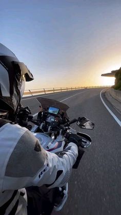 a person riding on the back of a motorcycle down a curvy road at sunset