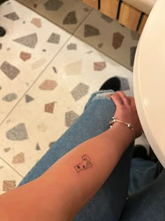 a person with a small tattoo on their arm sitting next to a white toilet bowl