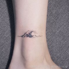 a small wave tattoo on the ankle is shown in black and grey colors, with an ocean wave coming out of it