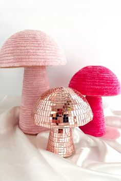 two pink and one red mushroom lamps on a white cloth covered tablecloth, with the light reflecting off of them