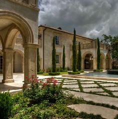 a large stone building with trees and flowers in the foreground, on a cloudy day