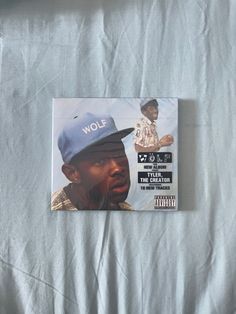 the album is laying on a bed with white sheets and blue cap covering it's head