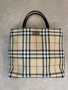 Vintage Burberry Nova Check top handle tote. Authentic. Preloved. Very good condition. Classic Nova Check canvas body. Brown leather handles. Slight discolouration around Burberry label on the outside. Magnetic snap closure. Canvas lined on the inside. One zipper interior pocket. Comes with original dust bag. Made in Italy. Measures 28.5cm length x 10cm width x 26cm height. Handles drop 10cm. Burberry Top, Burberry Purse, Check Tops, Purse Vintage, Top Handle Bags, Vintage Burberry, Leather Handles, Leather Handle, Snap Closure