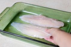 two raw fish fillets sitting in a green pan on a counter top, being held by someone's hand