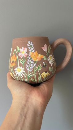 a hand holding a brown and white flowered mug