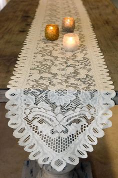 two candles are sitting on top of a table with lacy doily and lace runner