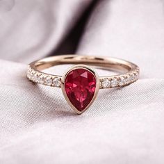 a red heart shaped diamond ring on top of a white cloth with diamonds around it