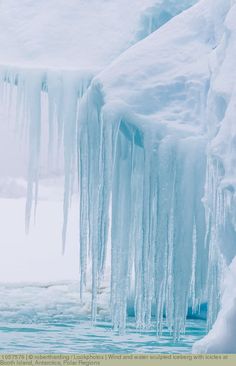 ice hanging from the side of a frozen cliff next to a body of water with icicles on it