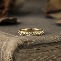 a gold wedding ring sitting on top of a wooden table next to an old book