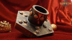 an old metal vase sitting on top of a red cloth next to a pine cone