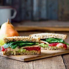 a sandwich is cut in half on a cutting board next to an apple and pear