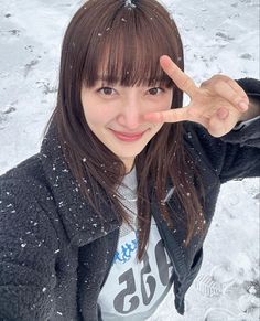 a young woman making the peace sign with her fingers in the snow while wearing a black jacket