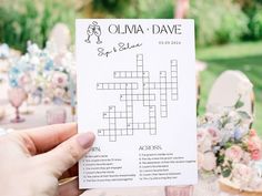 a person holding up a crossword puzzle piece in front of a table with flowers