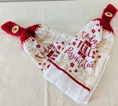 two red and white kitchen towels on top of a tablecloth with embroidered sayings