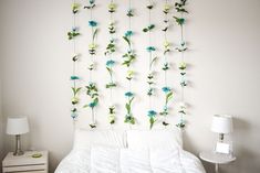 a bed with white sheets and blue flowers hanging from the headboard, next to a night stand