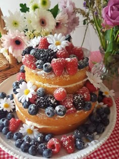 a three tiered cake covered in berries and blueberries on top of a checkered table cloth