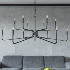 a modern chandelier hangs over a gray couch with apples on the coffee table