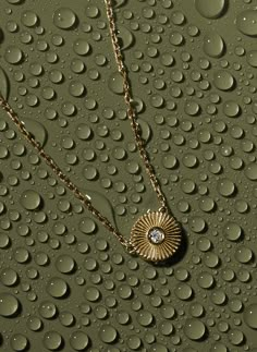 a close up of water droplets on a surface with a gold necklace and diamond pendant