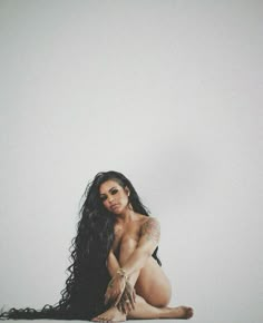 a woman with long black hair sitting on the floor in front of a white wall