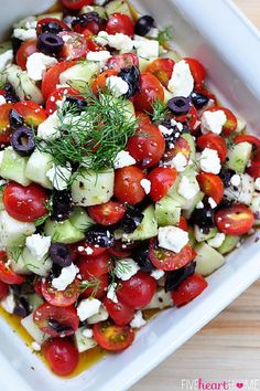 a white plate topped with a salad covered in feta cheese and cherry tomatoes on top of a wooden table