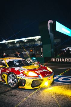 a red and yellow race car is parked on the side of the road at night