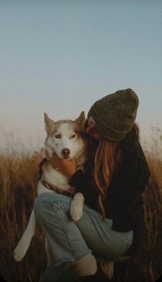 a woman holding a husky dog in her lap while sitting on top of a grass covered field