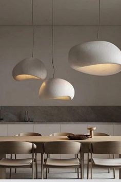 three white lights hanging from the ceiling above a dining room table with chairs and tables