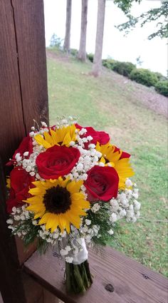 a bouquet of sunflowers and red roses in a vase on a wooden bench