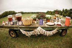 a picnic table with food and drinks on it in the middle of a grassy field