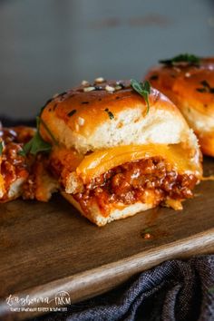 three sloppy joe sliders sitting on top of a wooden cutting board