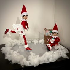 two elf dolls sitting on top of a table in front of a pile of white foam