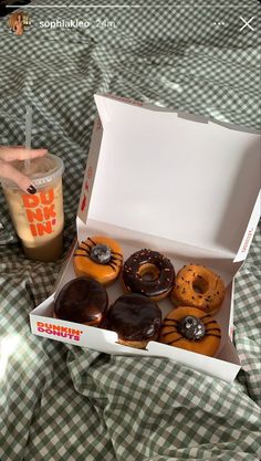 an open box of donuts sitting on top of a bed next to a drink