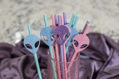 a glass filled with pink and blue straws next to an alien mask on top of a table