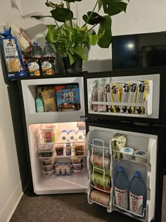 an open refrigerator filled with lots of food next to a potted plant on the floor