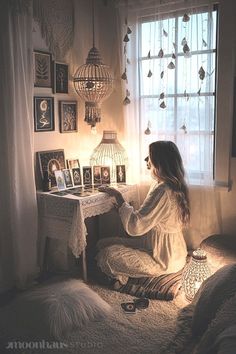 a woman sitting in front of a window next to a table with pictures on it