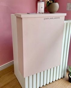 a pink wall with a white counter and potted plant on top in front of it