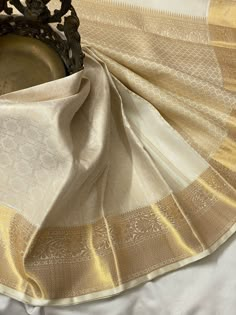 a white and gold cloth with a metal bowl in it's center, sitting on top of a bed