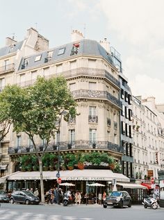 people are standing on the sidewalk in front of a building with many windows and balconies