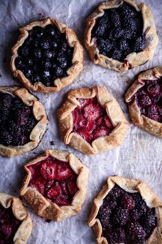 four pies with berries and blueberries in them on a piece of parchment paper