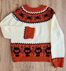 an orange and white knitted sweater with black cats on it, sitting on a wooden floor