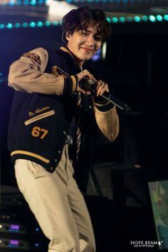 a man in a jacket and tie holding a microphone on stage with lights behind him