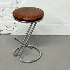 a small stool with a wooden seat and metal frame on concrete floor next to white brick wall