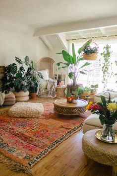 a living room filled with lots of furniture and plants on top of a wooden floor