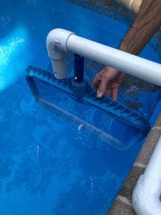 a man is cleaning the bottom of a blue pool with a white pipe and handrail