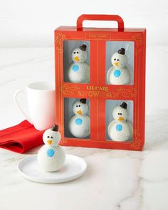 three snowmen are in a red box next to a cup and saucer