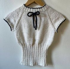 a white sweater with a black bow on the collar and sleeves, hanging from a wooden hanger