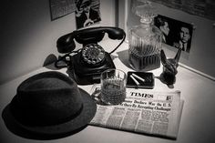 an old fashioned telephone, hat and other items sit on a table next to a newspaper