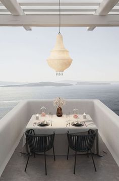 an outdoor dining area overlooking the ocean with two chairs and a table set for four