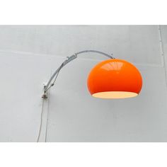 an orange light hanging from the side of a white wall next to a gray lamp